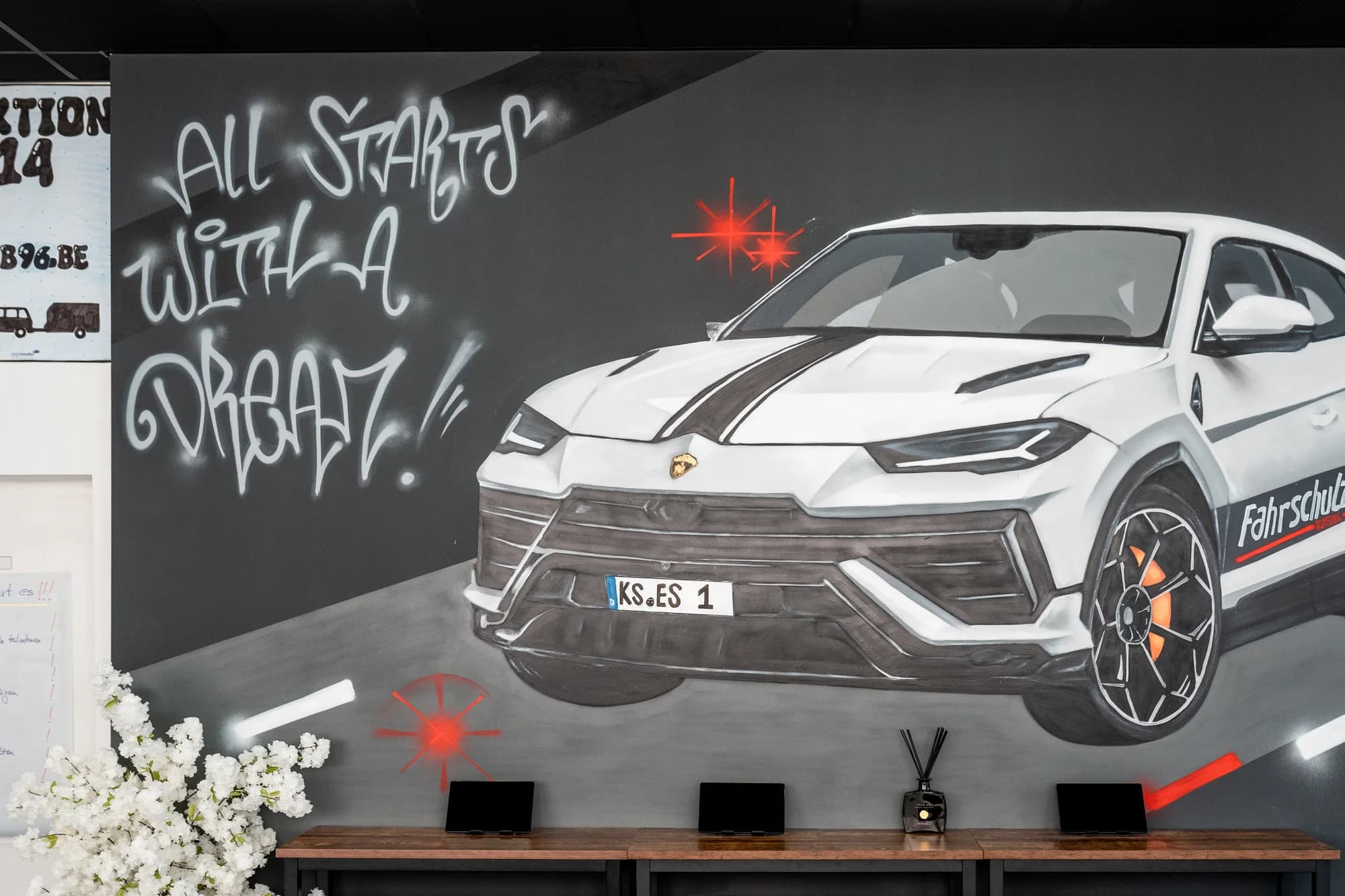 Wandbild im Empfang des Fahrschulzentrums Kassel: ein weißer Lamborghini Urus mit dem Schriftzug Fahrschulzentrum und dem Spruch All starts with a dream.